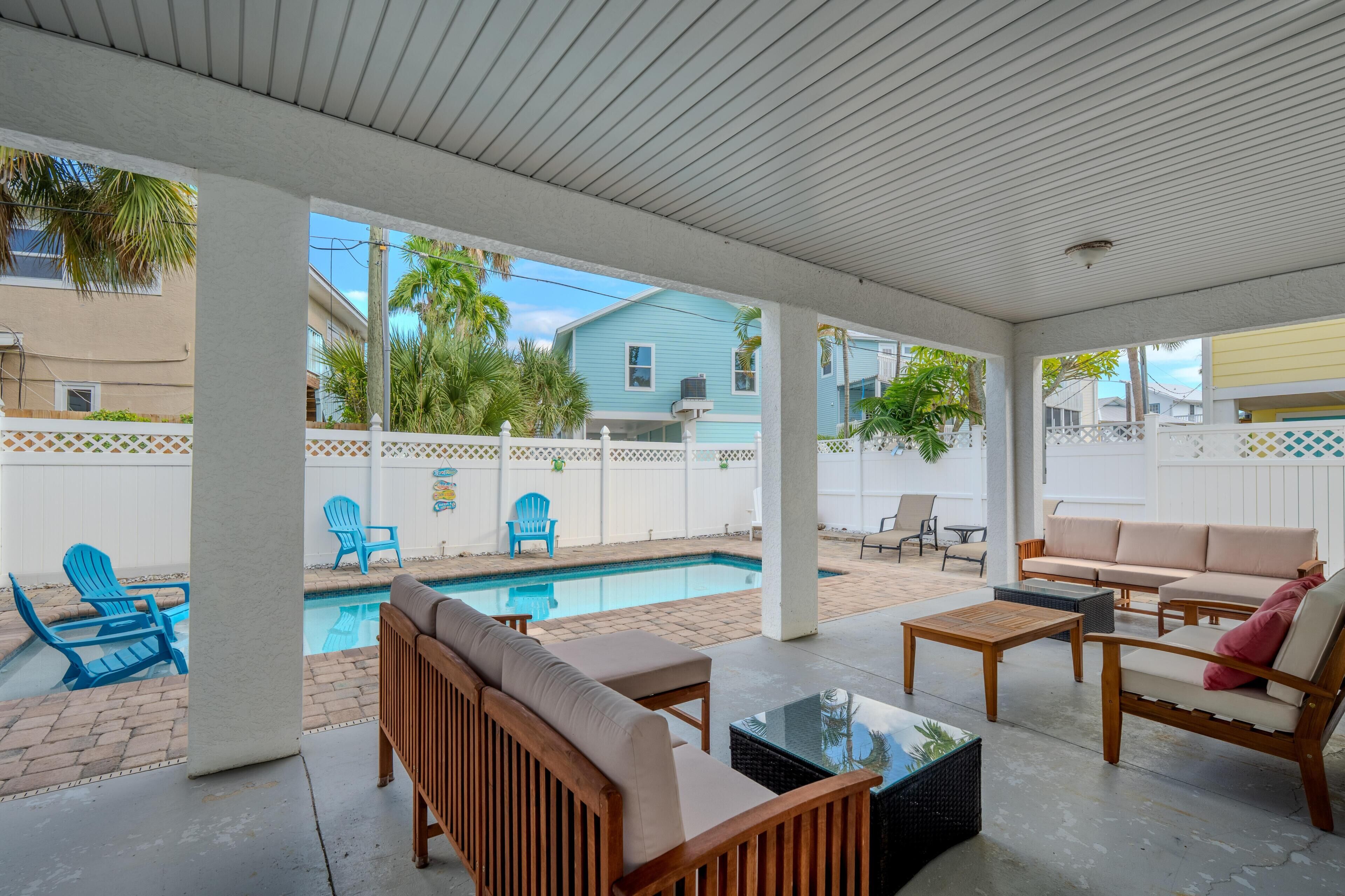 A covered outdoor area with a pool, seating, and a view of neighboring houses.