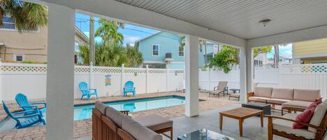 A covered outdoor area with a pool, seating, and a view of neighboring houses.