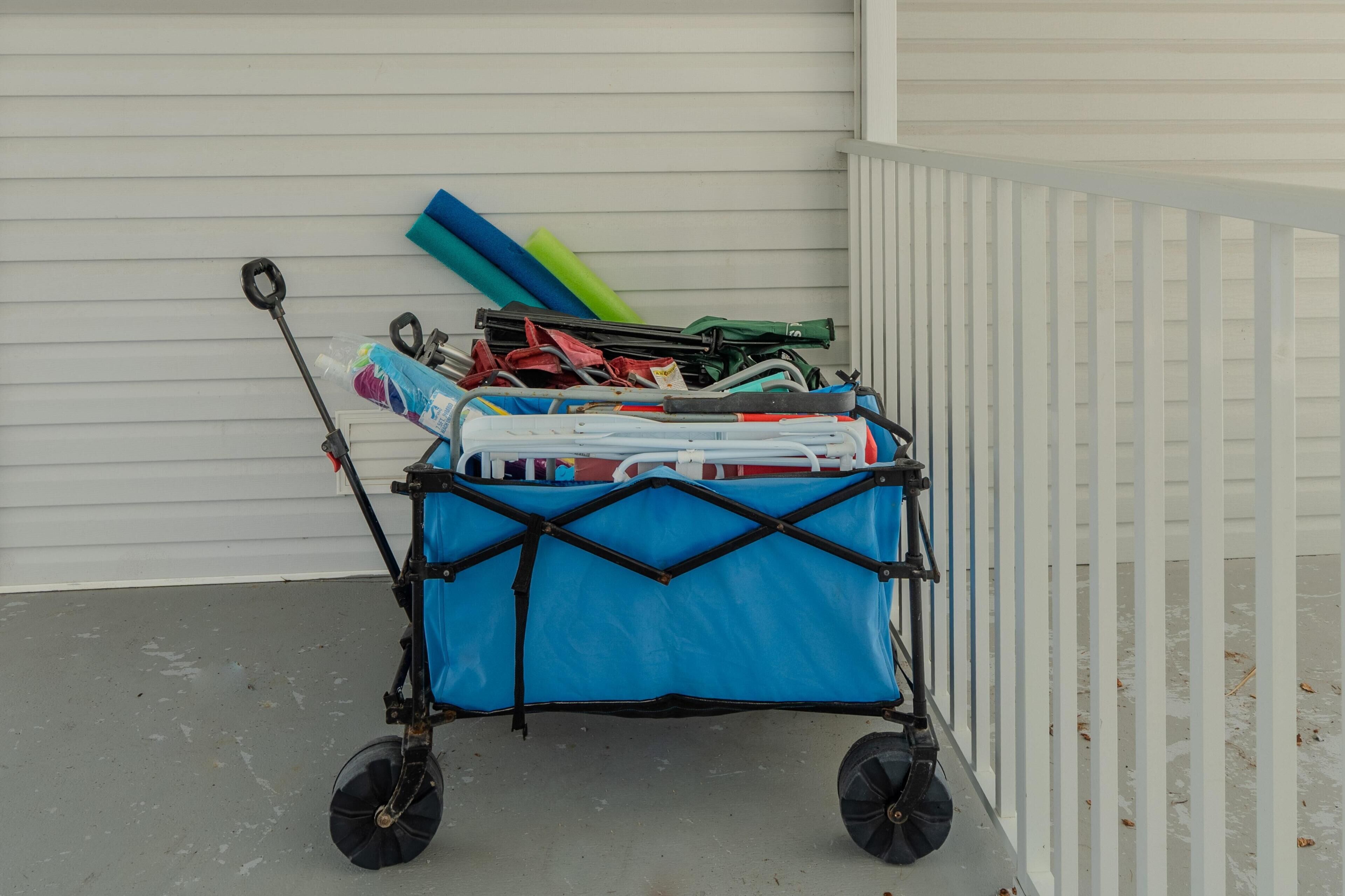 Un chariot bleu à roulettes, posé sur une surface en béton, et chargé de divers objets, notamment un tapis vert et bleu, un objet rouge et noir, ainsi que d’autres articles divers.