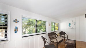 A room with two windows, white walls, and a wooden floor. There are two wicker chairs and a small table. - The Lazy Place (Fort Myers Beach)