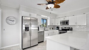 A modern kitchen with white cabinetry, stainless steel appliances, and a central island. - The Lazy Place (Fort Myers Beach)