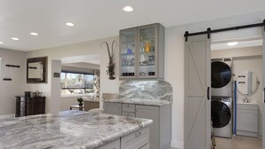 A modern kitchen with a marble countertop, grey cabinetry, and a sliding barn door leading to a laundry area. - Happy Daze (Fort Myers Beach)