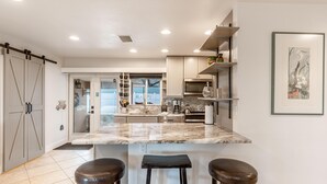 A modern kitchen with a marble countertop, two bar stools, and a large island. - Happy Daze (Fort Myers Beach)