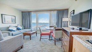Habitación de hotel con sofá, una mesa de comedor, televisión y vista al mar.