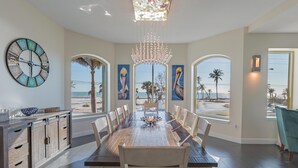 A dining area with a large wooden table, white chairs, a chandelier, and a clock on the wall. - Sabal Palms (Fort Myers Beach)