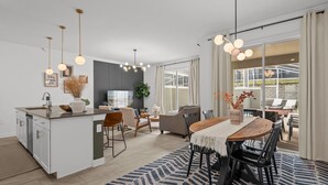 A modern kitchen with a central island, dining area with a wooden table and chairs, and a view of the outdoors through large windows. - Amazing 4 Bedrooms Home With Pool Close to Disney (Davenport)