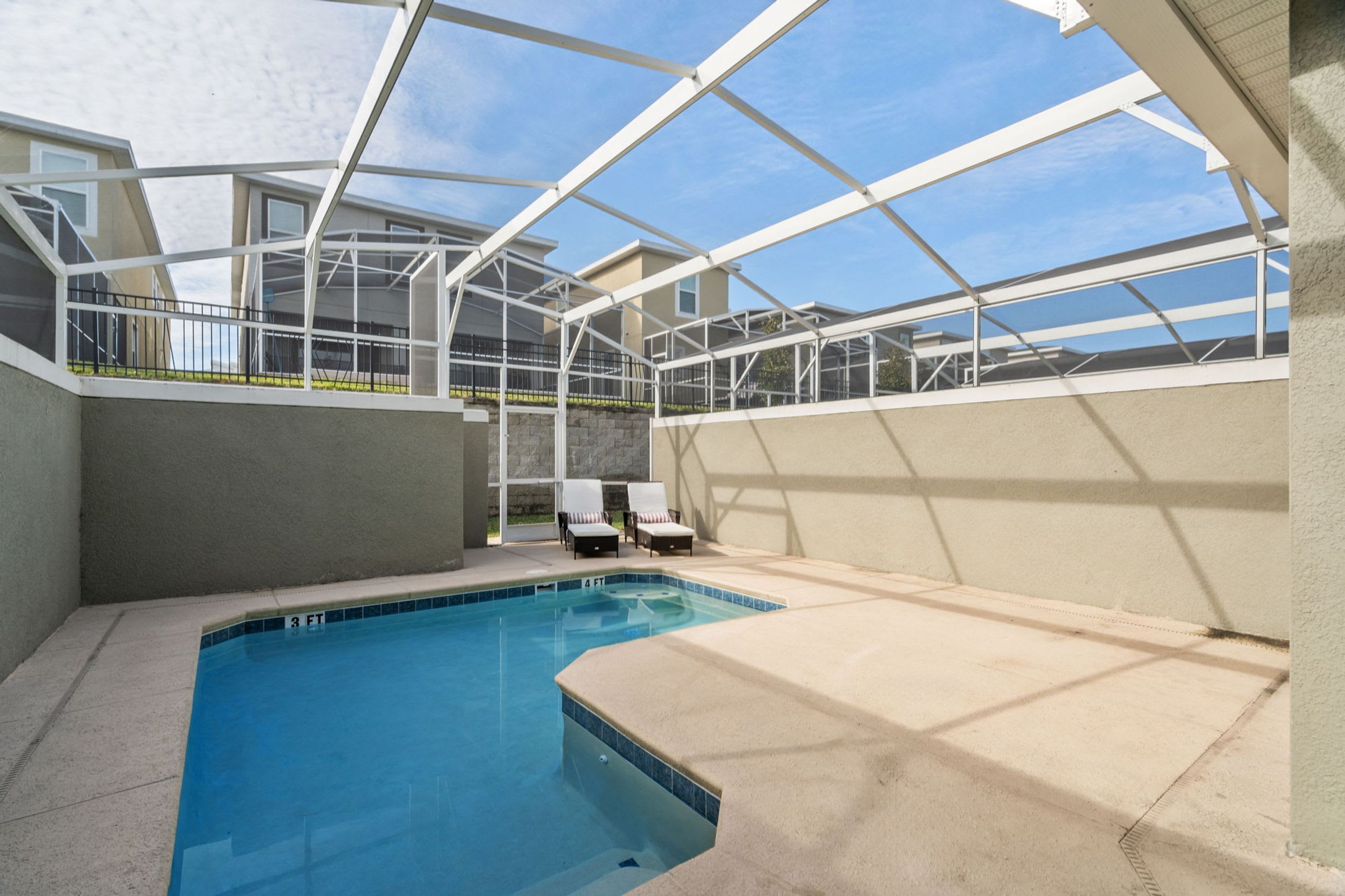 A swimming pool with a glass enclosure, lounge chairs, and a view of the surrounding buildings.