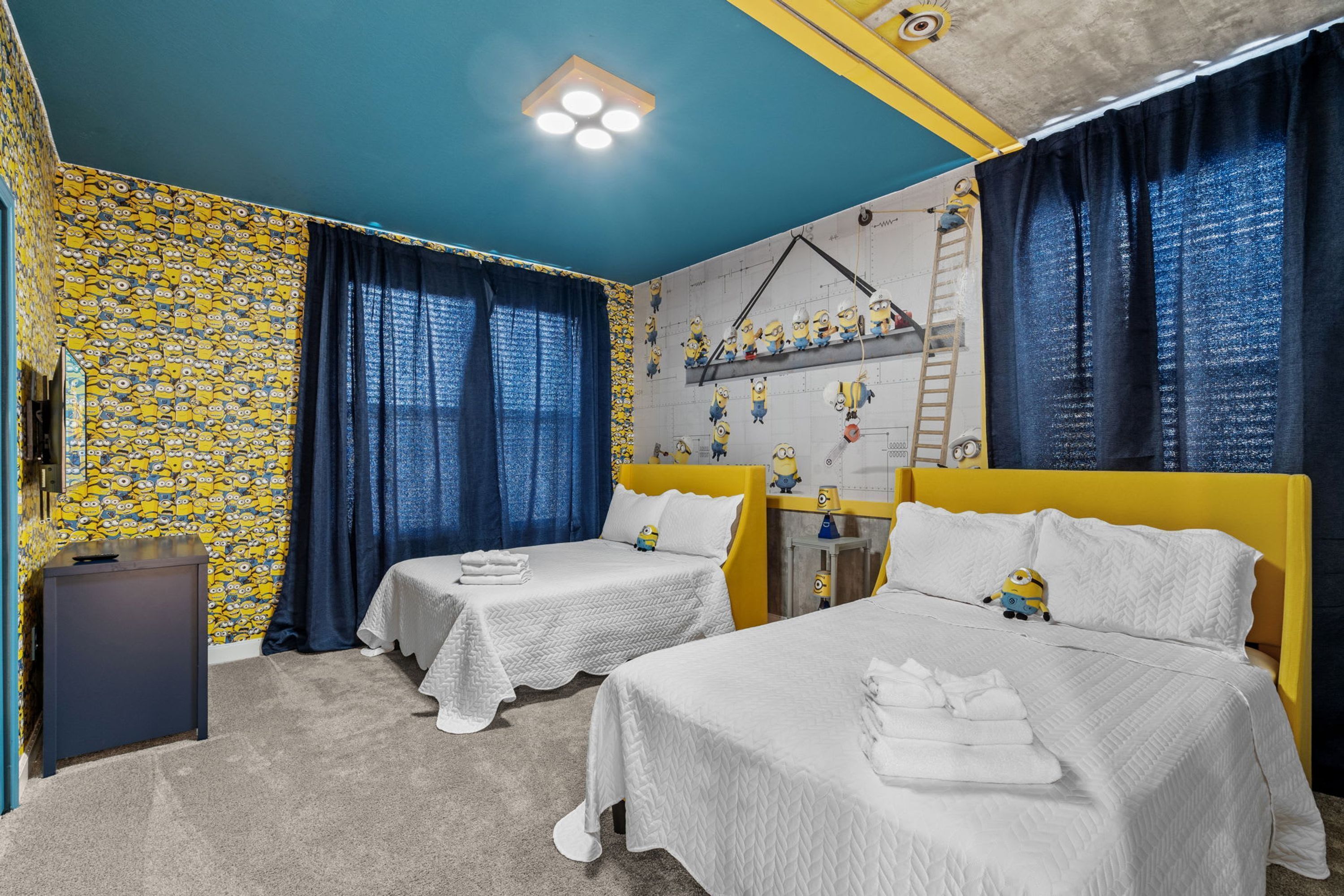 Una habitació amb dos llits, un escriptori i una paret decorada amb figures de Minions.