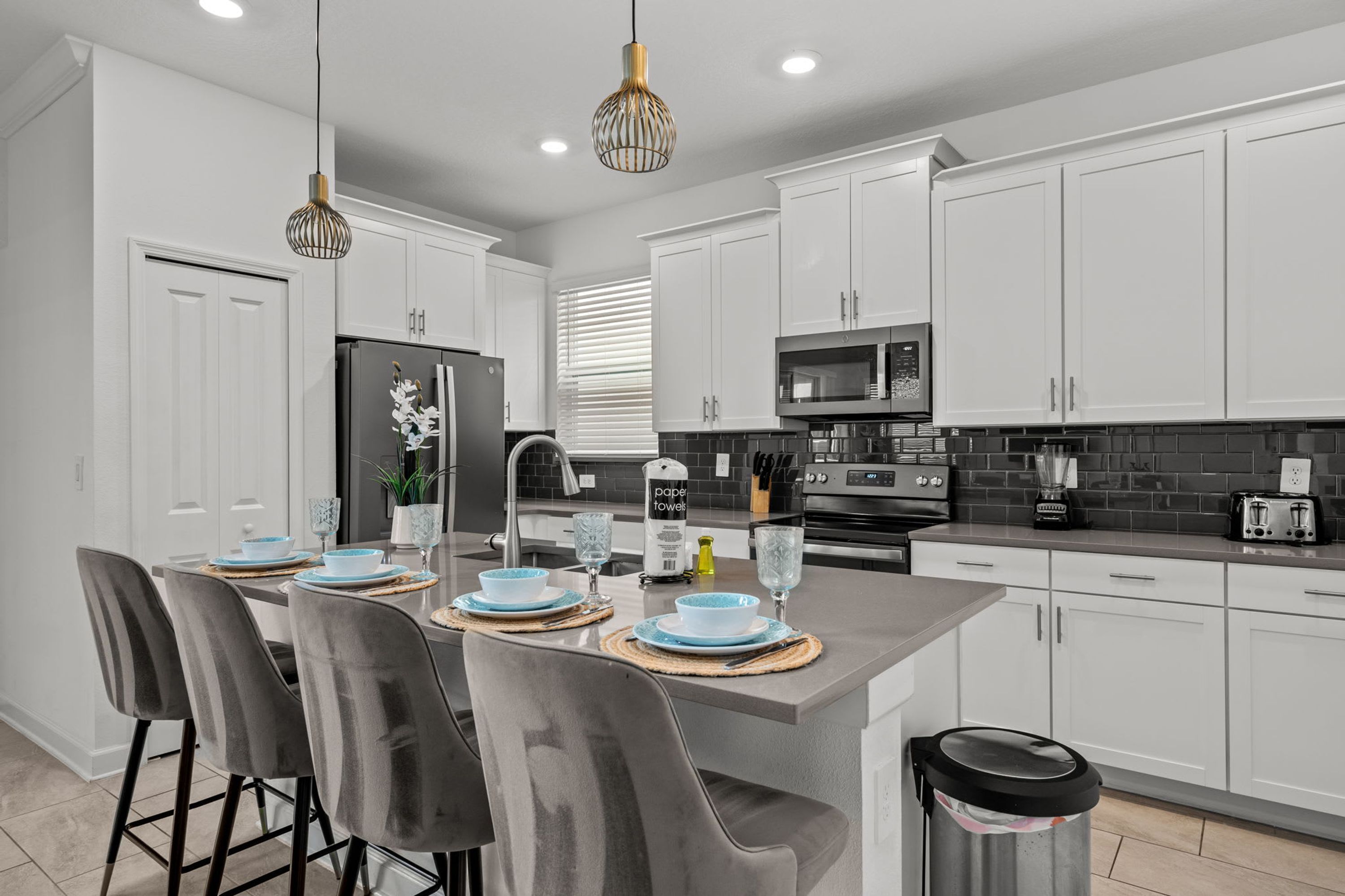 Una cocina moderna con armarios blancos, una isla central con taburetes, un refrigerador, un microondas y un lavabo.