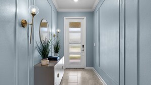 A hallway with light blue walls, a white door with frosted glass panels, a potted plant, and a wall-mounted light fixture. - Luxury 5bed Home With Pool and Game Room (Davenport)