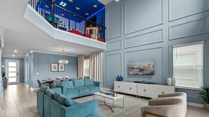 A spacious living room with a large sectional sofa, a coffee table, and a pink armchair. There is a dining area with a table and chairs, and a staircase leading to an upper level. - Luxury 5bed Home With Pool and Game Room (Davenport)