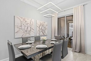 Un comedor moderno con una mesa rectangular dispuesta para seis comensales, flanqueada por sillas grises tapizadas. Encima de la mesa, hay dos cuadros abstractos en la pared.