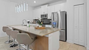 A modern kitchen with white cabinets, stainless steel appliances, a central island with bar stools, and pendant lighting. - Special 4bedroom TH w Private Pool Next to Disney (Davenport)