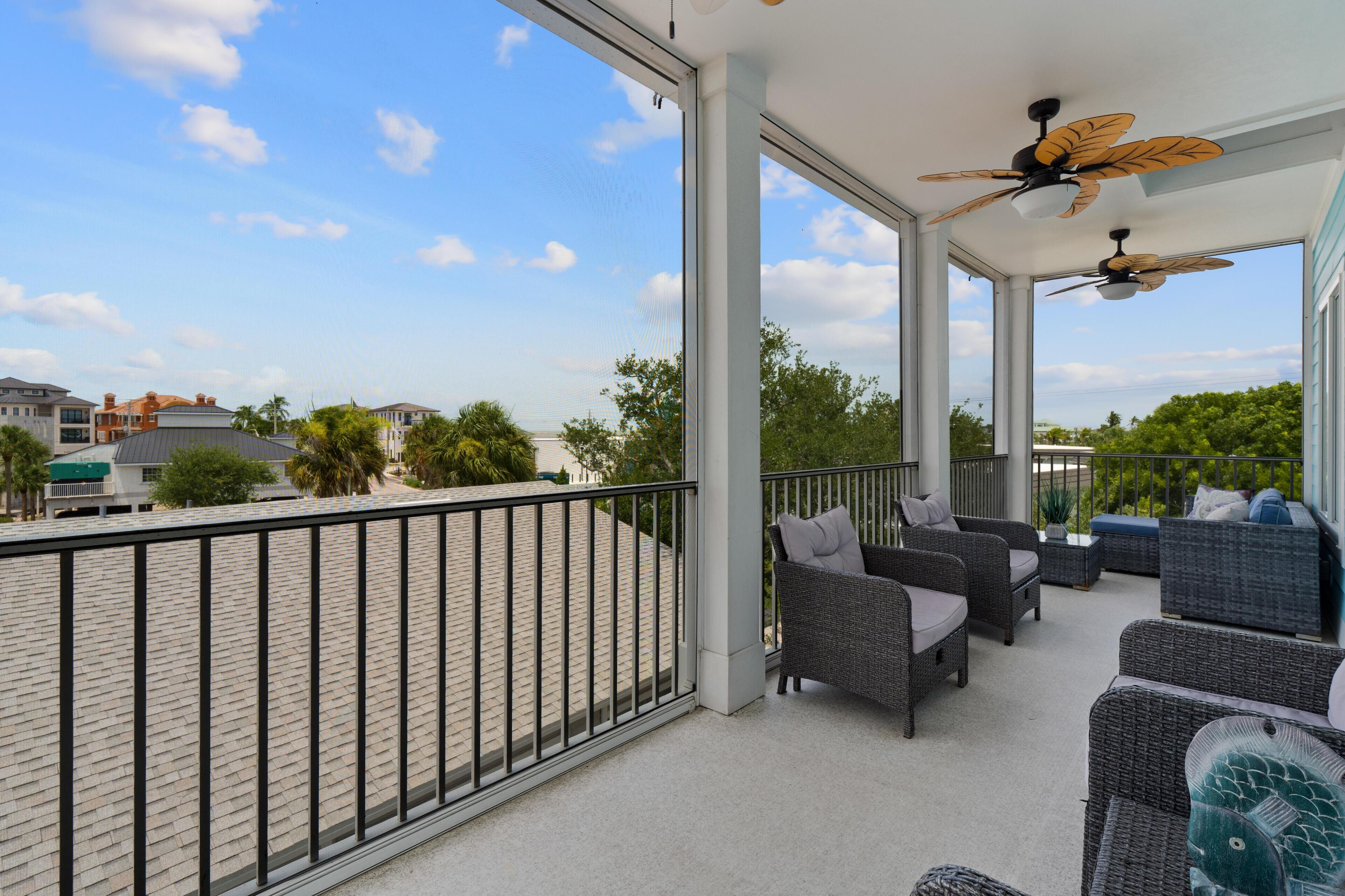 A covered outdoor balcony with wicker furniture and a ceiling fan.