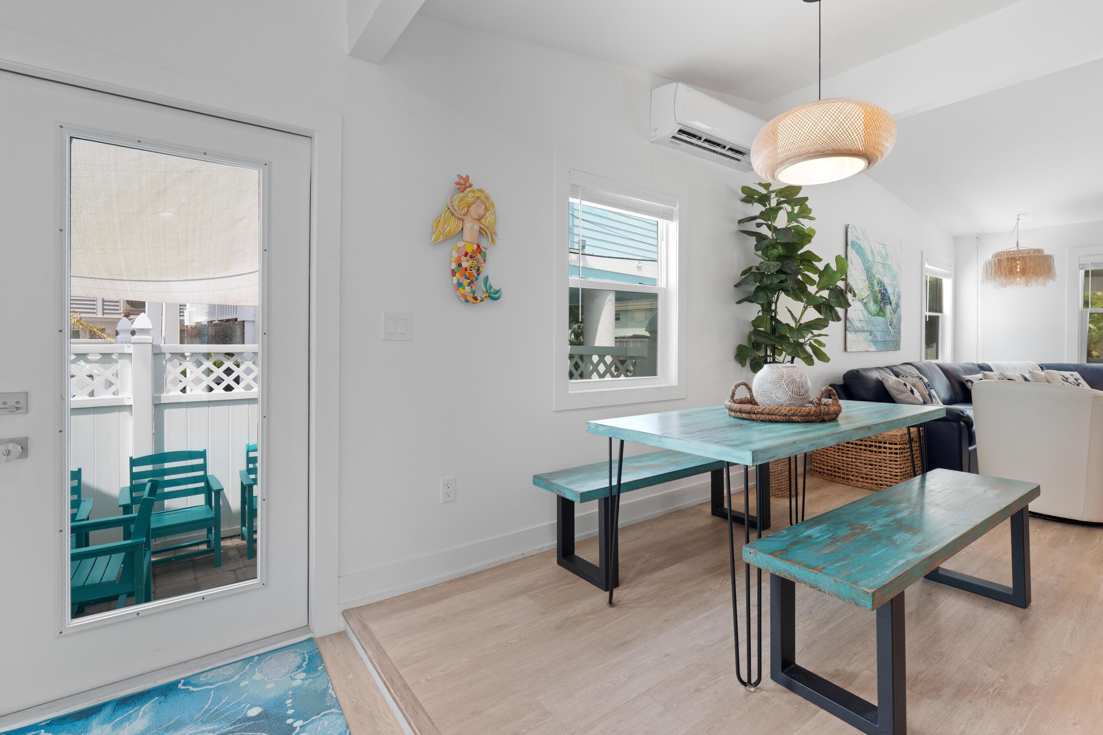 A modern interior with a dining area featuring a teal table and benches, a hanging light fixture, and a potted plant.