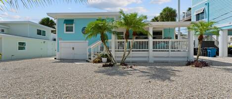 A beachfront property with a covered patio, palm trees, and a gravel driveway.