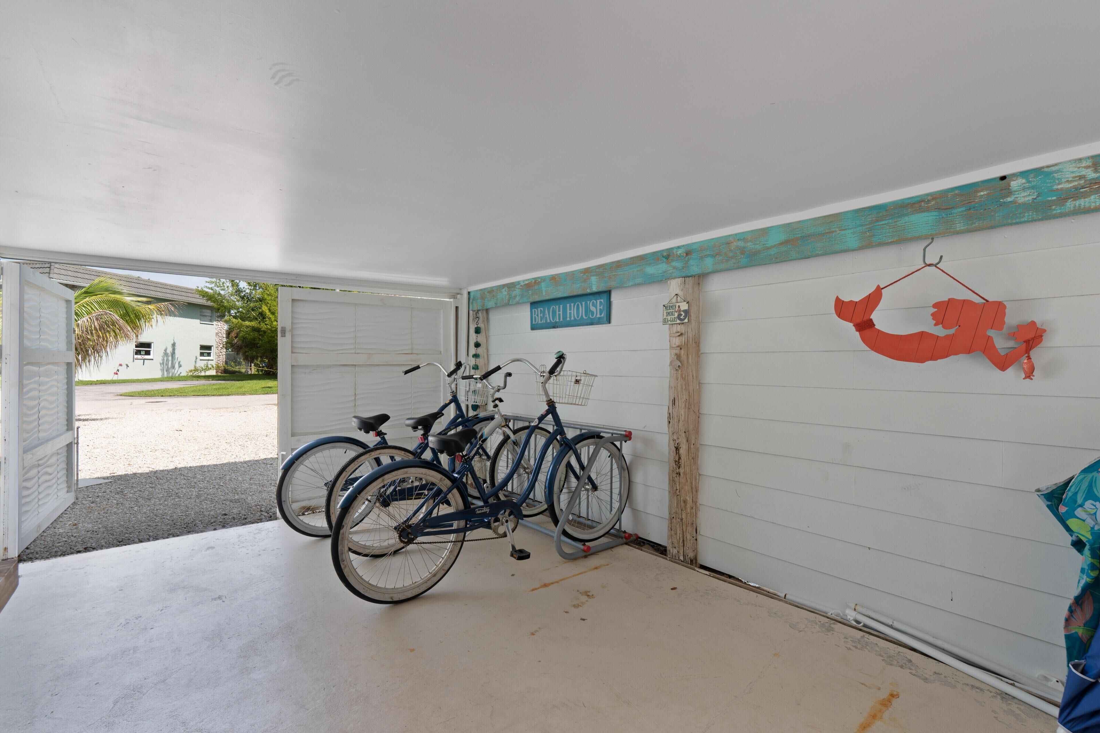 A garage with bicycles parked inside, a sign reading 'Beach House,' and a decorative fish hanging on the wall.
