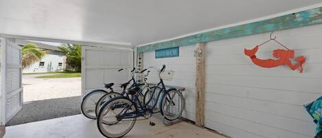A garage with bicycles parked inside, a sign reading 'Beach House,' and a decorative fish hanging on the wall.