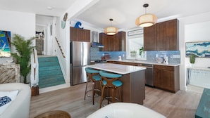 Una cocina moderna con una isla central, taburetes de bar, electrodomésticos de acero inoxidable y armarios de madera.