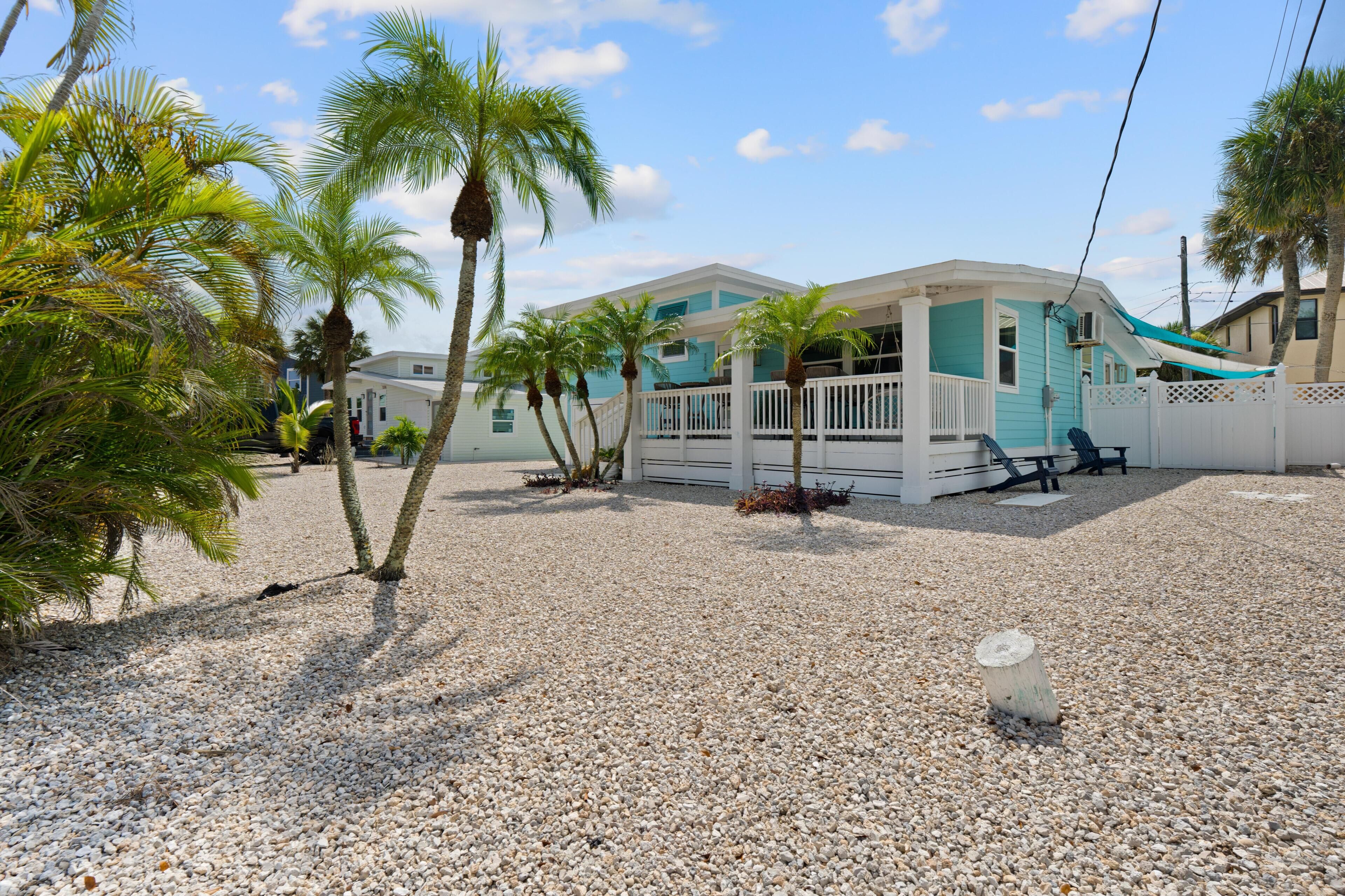 Una propiedad frente a la playa con una casa blanca y azul, palmeras y un camino de entrada de grava.