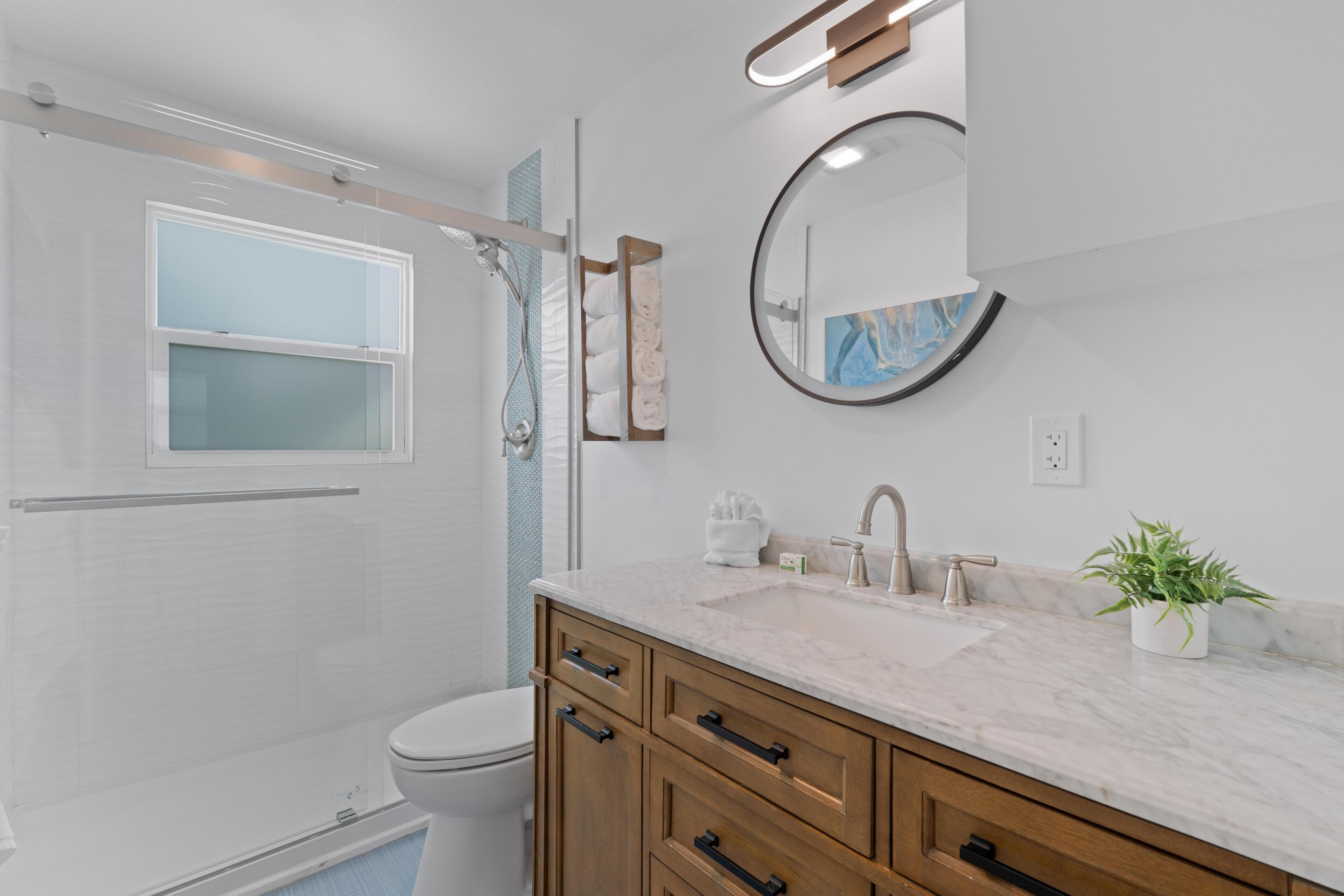 A modern bathroom with a shower, toilet, vanity with a sink, and a mirror.