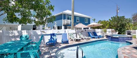 A swimming pool with a tiled edge, a blue house, and a white fence.