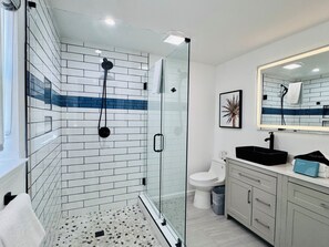 A modern bathroom with a glass shower enclosure, white and blue tiled walls, a white toilet, and a vanity with a mirror. - Ultimate coastal retreat! (Panama City)
