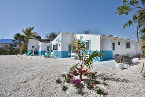 A two-story building with a white and blue exterior, a small garden with colorful flowers, and outdoor seating. - MT Sandy Haven #3 (Fort Myers Beach)