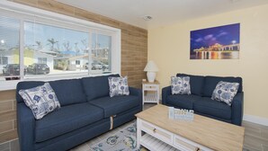 A living room with two dark blue sofas, a wooden coffee table, and a painting of a bridge at night on the wall. - MT Sandy Haven #3 (Fort Myers Beach)