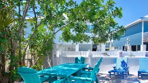 A turquoise outdoor dining area with a pool, surrounded by a white fence and trees. - MT Wind Swept #5 (Fort Myers Beach)