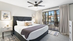 Ein modernes Hotelzimmer mit einem großen Bett, einem Deckenventilator, einem Balkon mit Aussicht und einem Nachttisch mit Lampe.