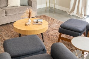 Un salon avec une table basse ronde en bois, un canapé gris et des fauteuils assortis de la même couleur.