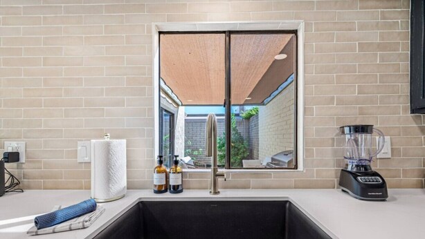 Eine moderne Küche mit einem großen Spülbecken, einem Fenster mit Außenblick und einem Mixer auf der Arbeitsfläche.