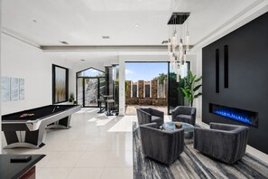 Un salon moderne doté d’une table de billard, de sièges confortables, d’une cheminée et offrant une vue sur l’extérieur.