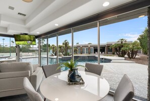 A modern indoor space with a pool, large windows, and a table with chairs. - Desert Diamond HTD Pool/Hot Tub/Tennis/BBall/Sauna (Scottsdale)
