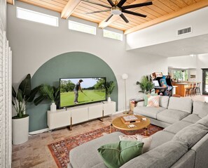 A modern living room with a large flat-screen TV, a sectional sofa, a coffee table, and a gaming area with arcade machines.