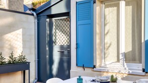 A dining area with a brick floor, white table, and chairs, set against a building with blue shutters and a white door. - Perfect location! Quiet fisherman's cottage / terrace, bbq, elec. bikes.  (Trouville-sur-Mer)