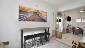 Ein modernes Wohnzimmer mit einer hölzernen Bank, einem großen Gemälde eines Piers und Blick in den angrenzenden Raum.
