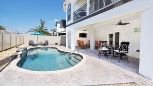 Ein Schwimmbecken mit gewölbter Kante, umgeben von einer Terrasse mit Stühlen und einem Tisch.