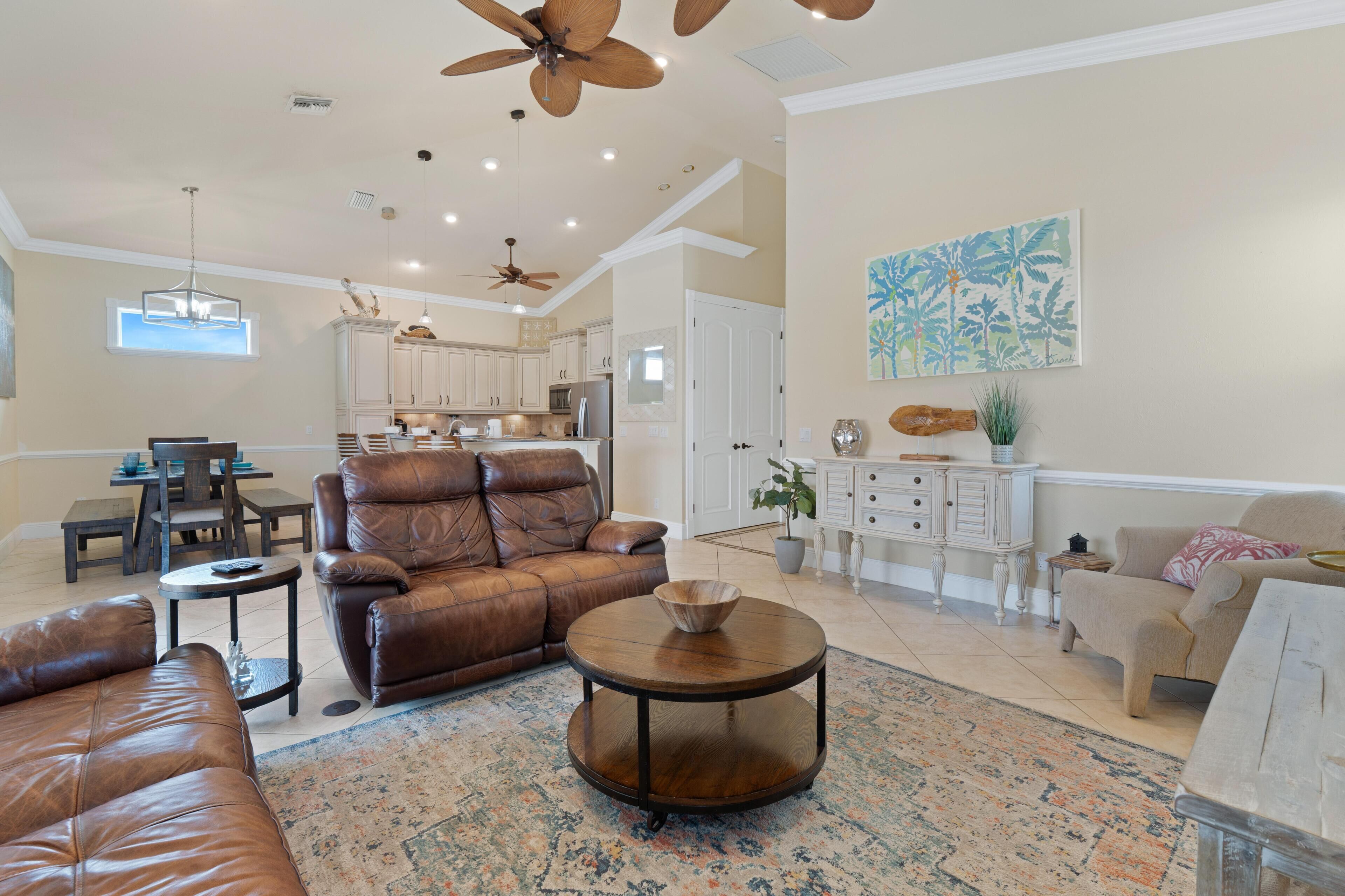 A spacious living room with leather furniture, a round coffee table, and a kitchen in the background.