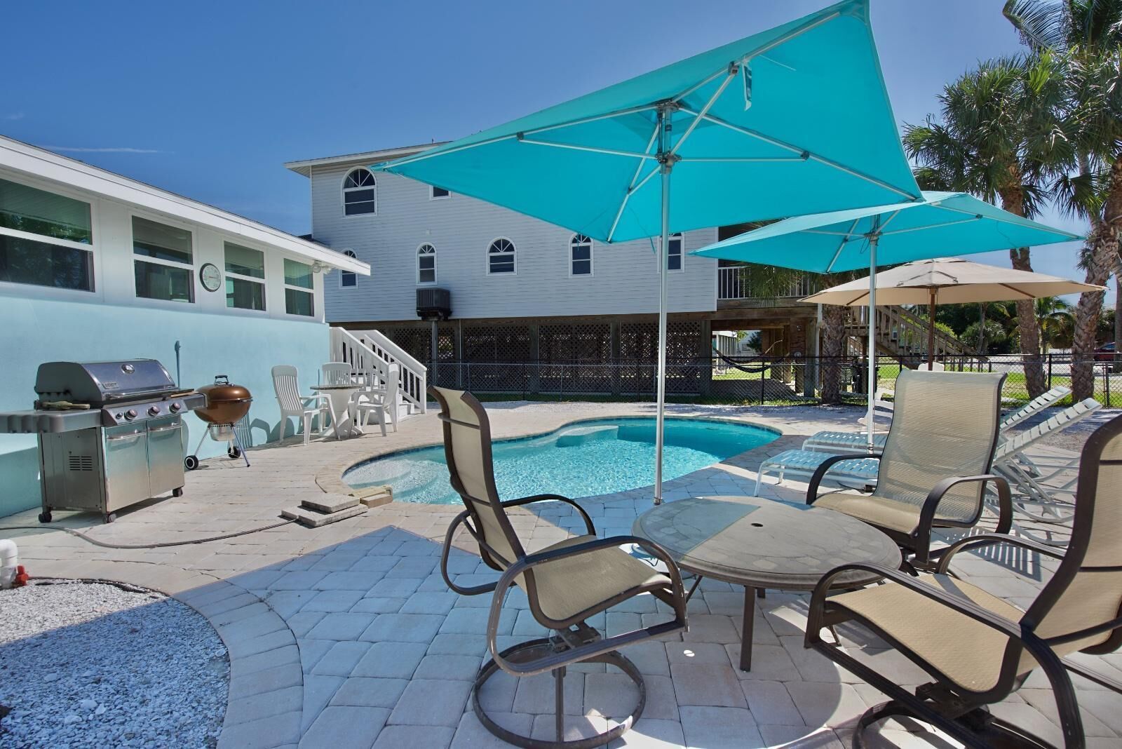 A poolside area with a barbecue grill, lounge chairs, and umbrellas.