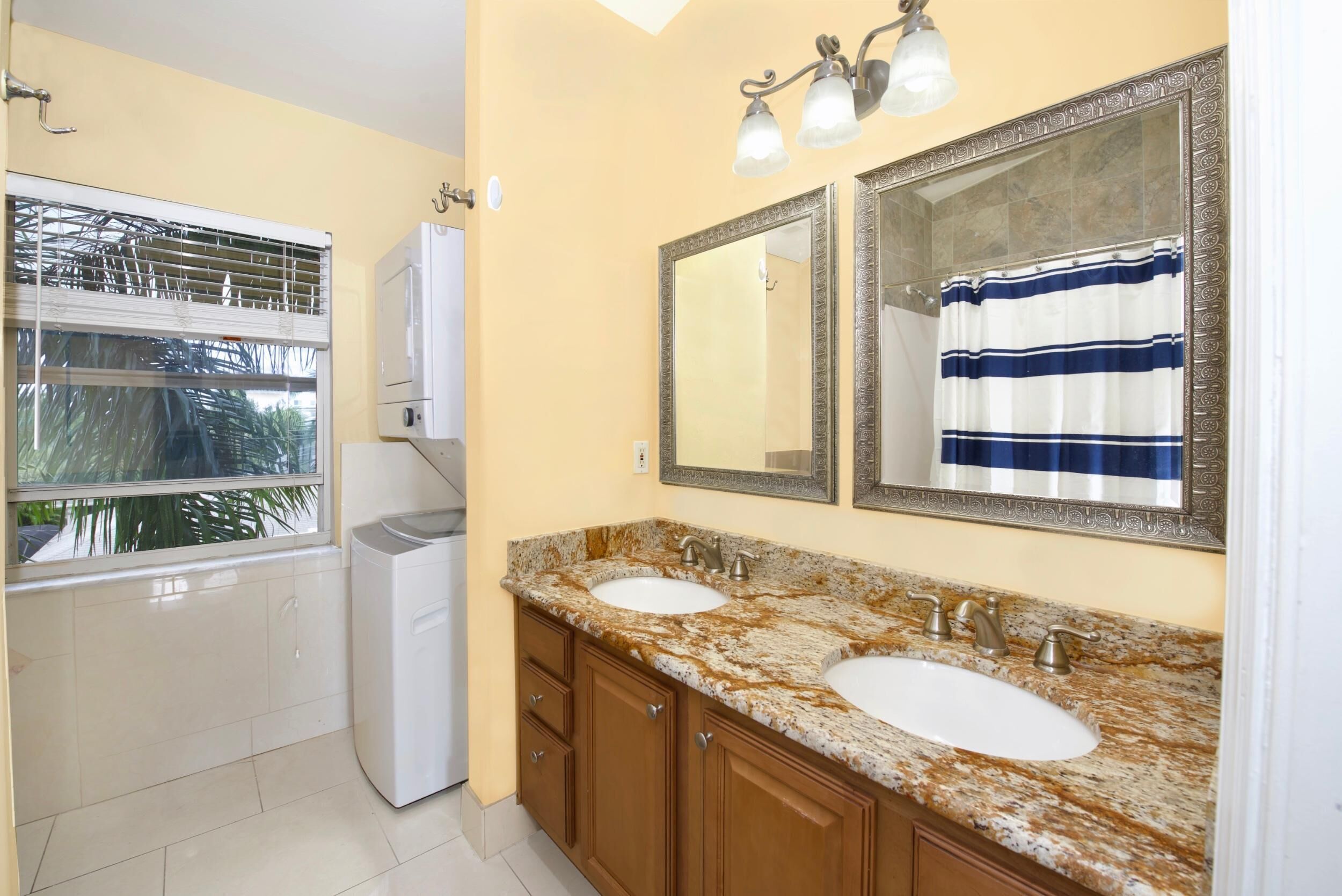 A bathroom with two sinks, a window, a washing machine, and a shower curtain.