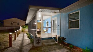 A house with a blue exterior, a front porch with steps, and a door leading to an interior space with a ceiling fan and a chair. - Casa Azul A (Fort Myers Beach)