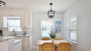 A modern kitchen with white cabinets, a wooden dining table with wicker chairs, and a hanging light fixture. - Casa Azul A (Fort Myers Beach)