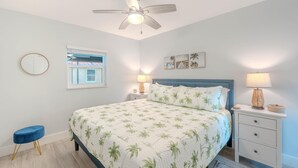 Quarto com cama, ventilador de teto, luminárias de cabeceira, mesa de cabeceira, espelho redondo e janela com vista.