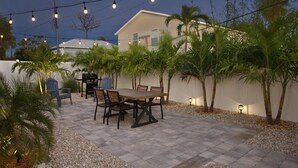 Um pátio externo com mesa e cadeiras, cercado por palmeiras e um cercado branco.