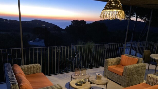 A balcony with wicker furniture, a table, and a hanging light fixture. - Casa Las Rocas (Begur) (Begur)