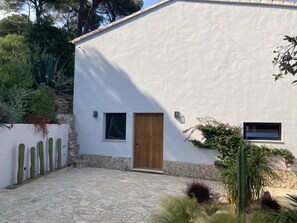 A white building with a wooden door, two windows, and a stone pathway.