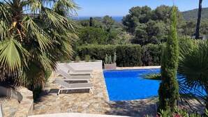A stone pool with lounge chairs, surrounded by greenery and a view of the sea. - Casa Las Rocas (Begur) (Begur)