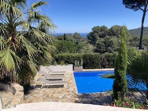 A stone pool with lounge chairs, surrounded by greenery and a view of the sea. - Casa Las Rocas (Begur) (Begur)
